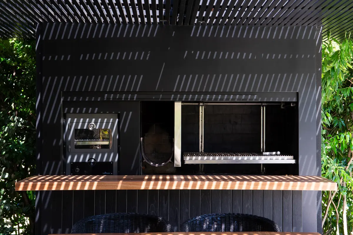 Área de churrasqueira externa moderna com estrutura de madeira e metal preto — projeto Quincho SA, por Estudio Junor, em Pilar